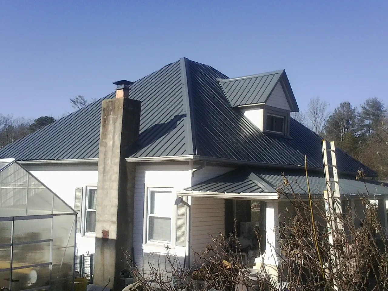 Dark blue standing seam metal roof on a white farmhouse with dormer — Slate & Tile Roof Repair by Roofing Brothers in Evadale
