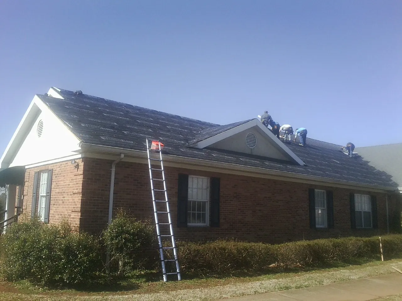 Crew tearing shingles off a brick ranch roof with a ladder set — Metal Roof Repair work by our crew in Evadale
