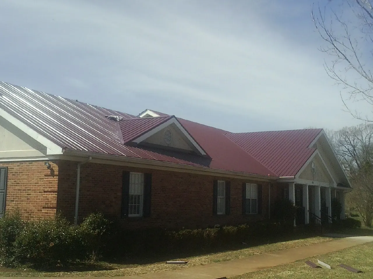 Red metal roof with gabled entries on a long brick building, from a Hail Damage Roof Repair job in Evadale