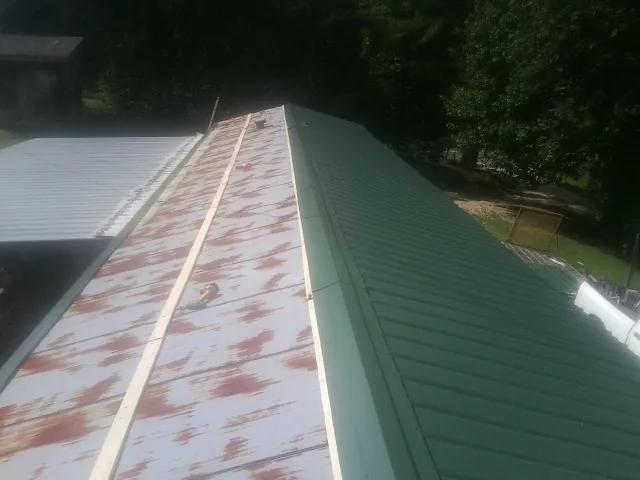 Old rusted panels beside newly installed green metal roofing — Wind Damage Roof Repair by Roofing Brothers in Evadale