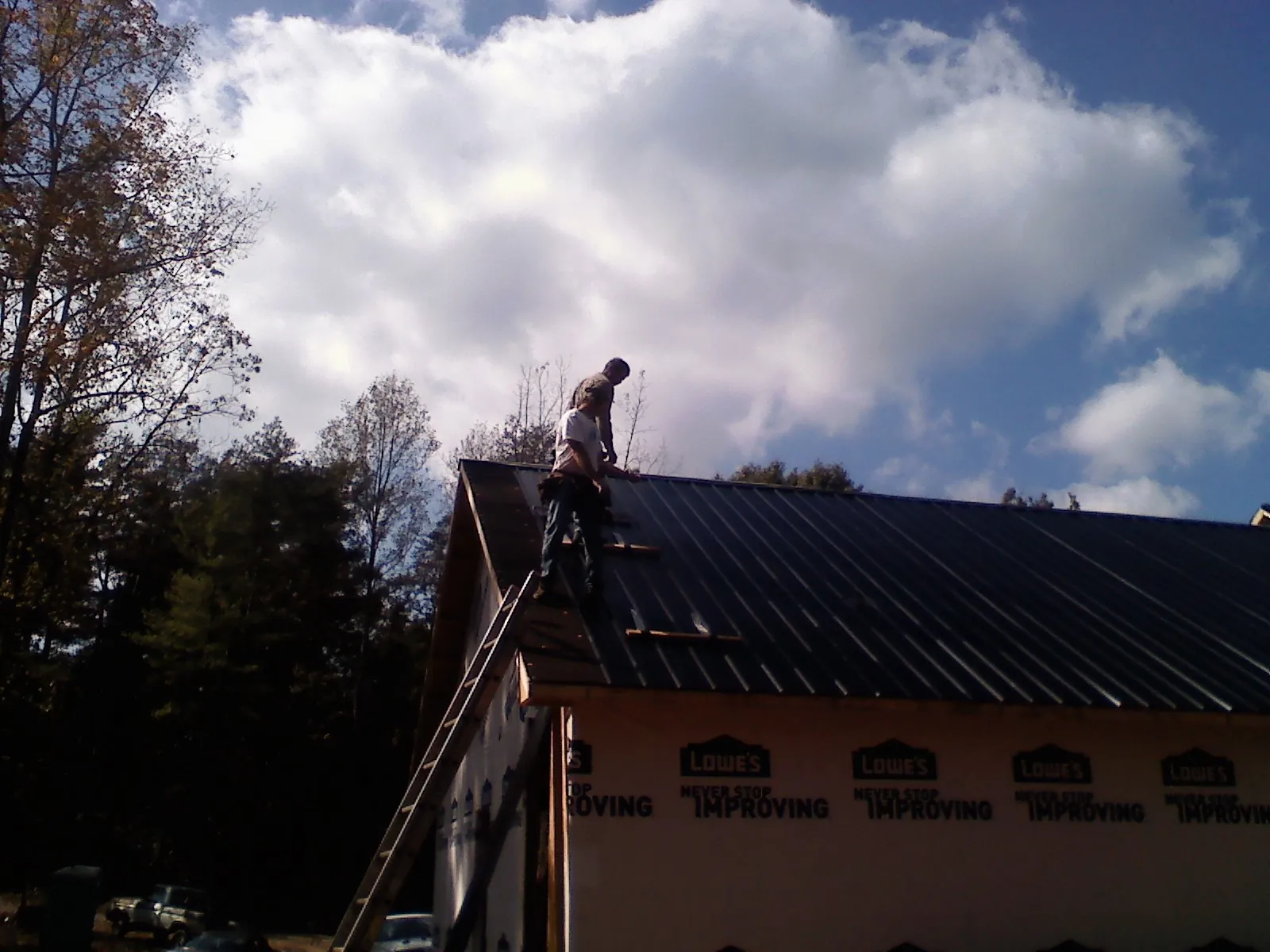 Roofer fastening dark metal panels high against a cloudy sky, from a Roof Inspection job in Evadale