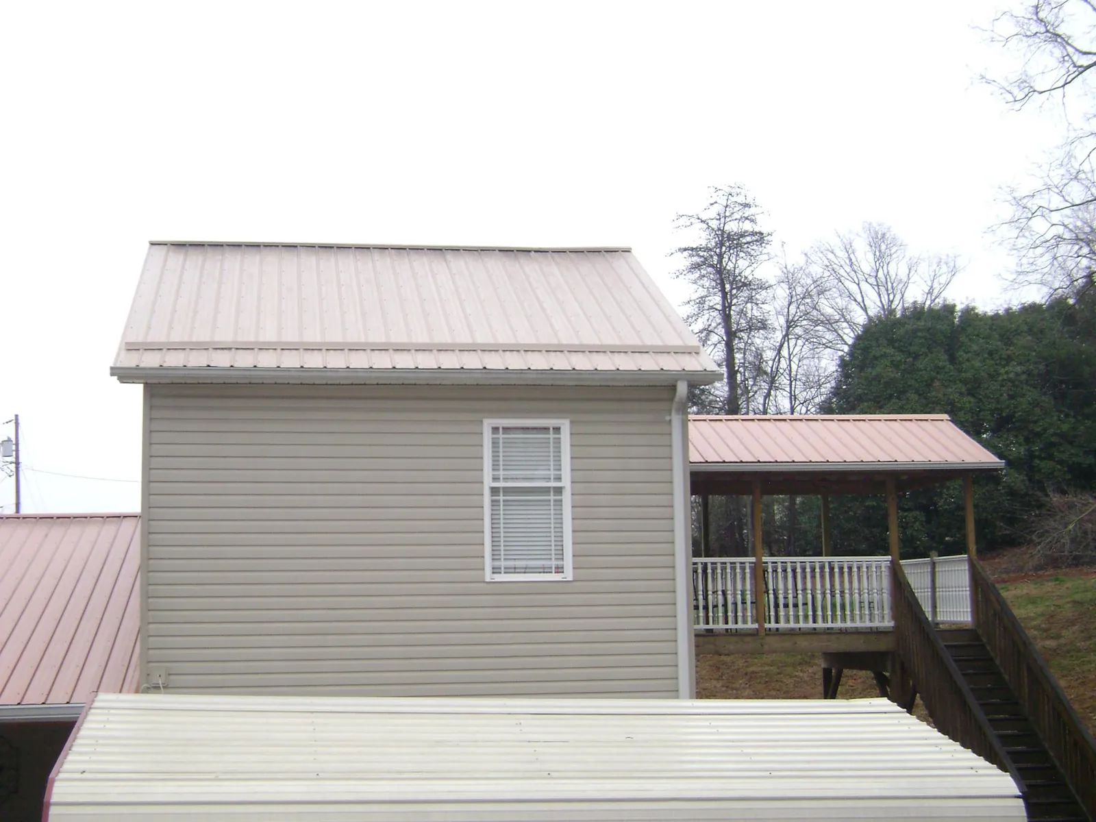 Tan metal roofs on a two story addition and attached porch, from a Roof Replacement job in Evadale